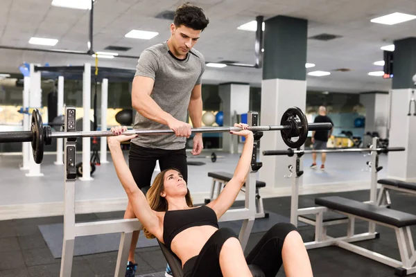 Treinador pessoal ajudando uma jovem mulher a levantar pesos — Fotografia de Stock