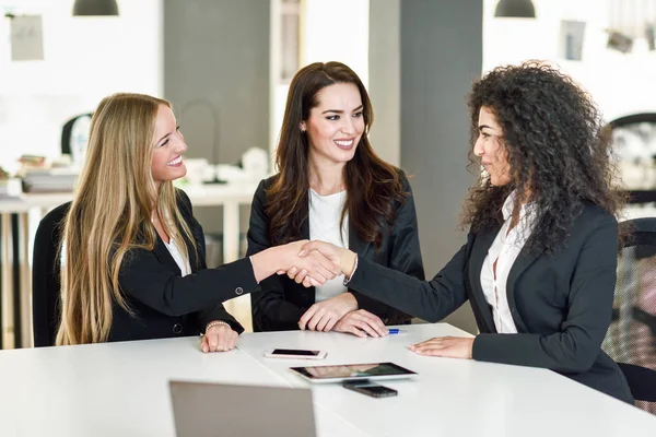 Three businesswomen shaking hands in a modern office — Stock Photo, Image