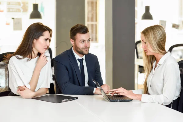 Blonde businesswoman explaining with laptop to smiling young cou — Stock Photo, Image