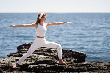 Genç kadın beyaz elbise giyen Beach yoga yaparken
