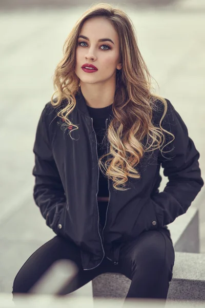 Bella ragazza che indossa giacca nera seduta in strada . — Foto Stock