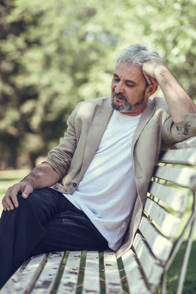 Pensive mature man sitting on bench in an urban park. — Stock Photo, Image