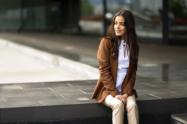 Junge Geschäftsfrau sitzt vor einem Bürogebäude in der Stadt — Stockfoto
