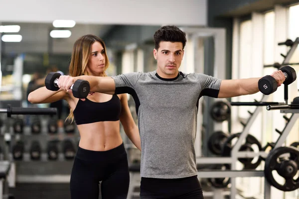 Persoonlijke trainer helpen van een jonge man die lift gewichten — Stockfoto