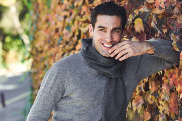 Мужчина в зимней одежде улыбается на фоне осенних листьев — стоковое фото