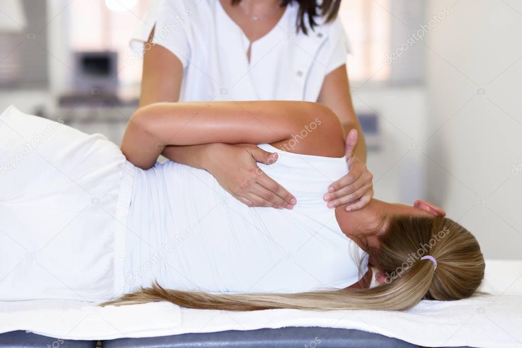 Professional female physiotherapist giving shoulder massage to b