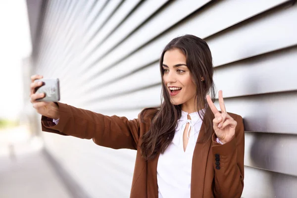 Young woman taking selfie photograph with smartphone doing V sig — Stock Photo, Image