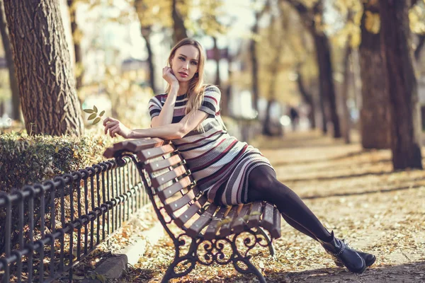 Mujer rubia joven sentada en un banco de un parque — Foto de Stock