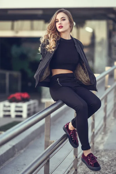 Beautiful young girl wearing black jacket sitting in the street. — Stock Photo, Image