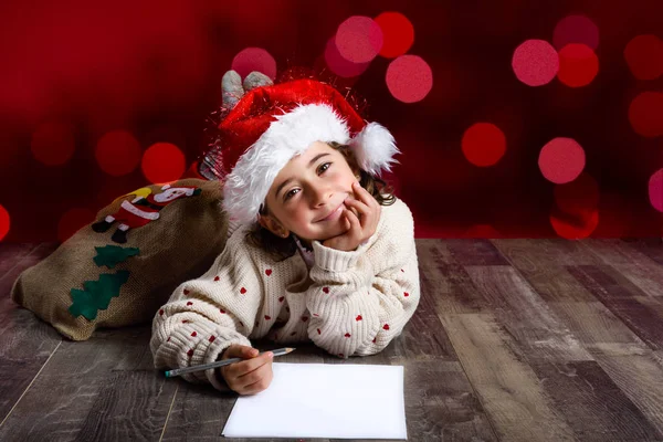 Очаровательная маленькая девочка в шляпе Санты пишет Санте письмо. — стоковое фото
