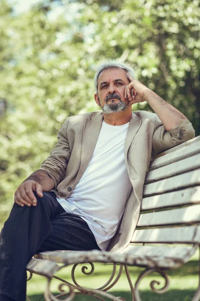 Pensive mature man sitting on bench in an urban park. — Stock Photo, Image