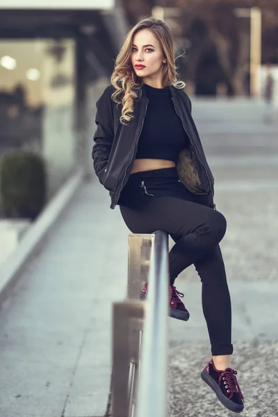 Красива молода дівчина в чорній куртці сидить на вулиці . — стокове фото