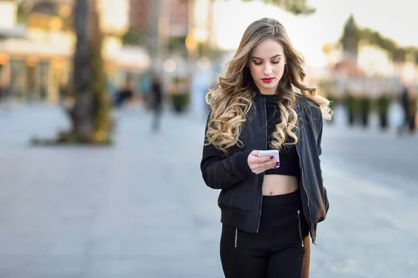 Mulher loira mensagens de texto com seu smartphone em fundo urbano — Fotografia de Stock
