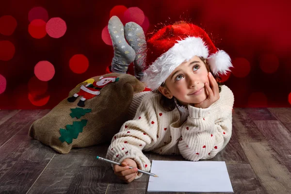 Очаровательная маленькая девочка в шляпе Санты пишет Санте письмо. — стоковое фото