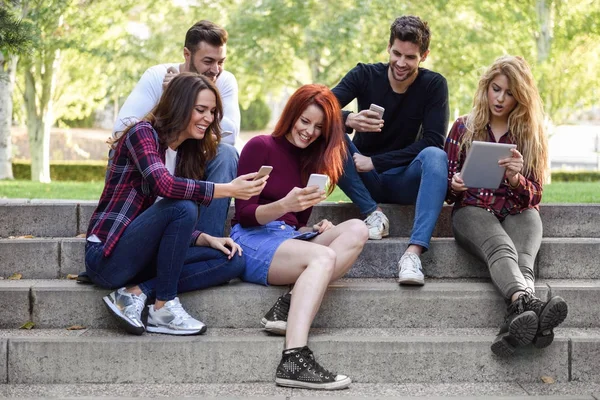 Jóvenes que usan teléfonos inteligentes y tabletas al aire libre — Foto de Stock