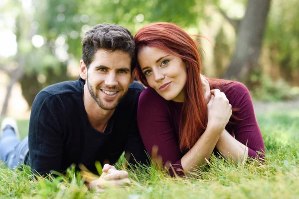 Belo jovem casal que coloca na grama em um parque urbano . — Fotografia de Stock