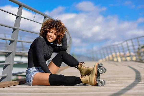 Afro frisyr kvinna på rullskridskor sitter på urban bridge — Stockfoto