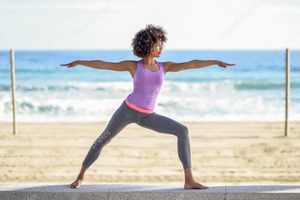 Black woman, afro hairstyle, doing yoga in warrior asana in the 