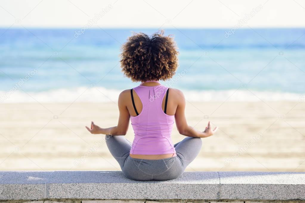 Black woman, afro hairstyle, doing yoga in the beach