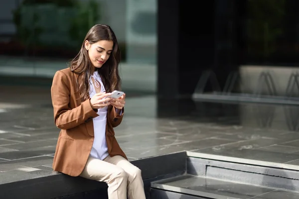 Empresaria de mensajes de texto con un teléfono inteligente al lado de un edificio de oficinas — Foto de Stock