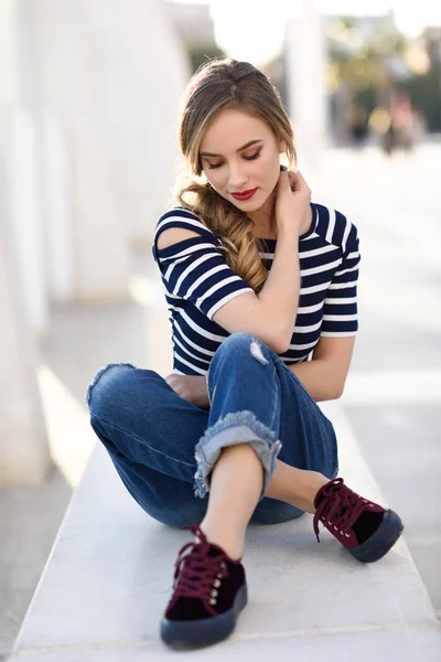 Femme blonde, mannequin de mode, assise en fond urbain . — Photo