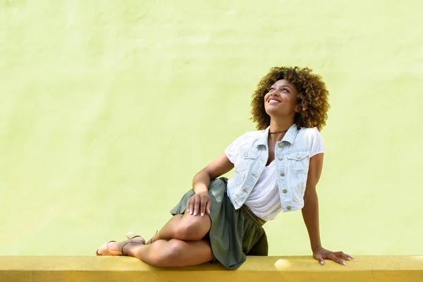 Ung svart kvinna, afro frisyr, sitter på en urban vägg — Stockfoto