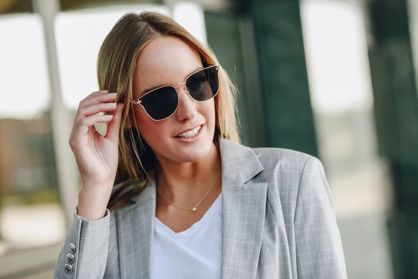 Beautiful young blonde woman with sunglasses in urban background — Stock Photo, Image