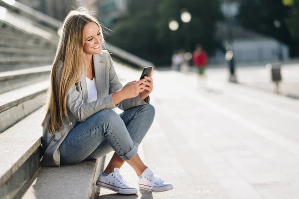 Mulher loira jovem bonita olhando para seu smartphone e smili — Fotografia de Stock