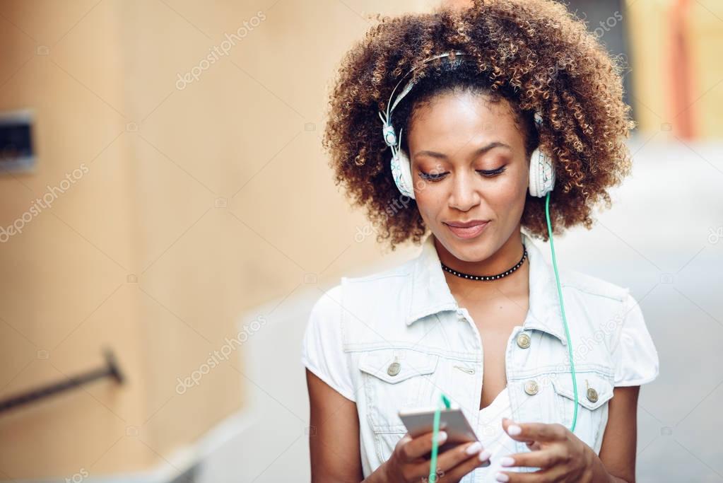 Black girl, afro hairstyle, in urban street with headphones and 