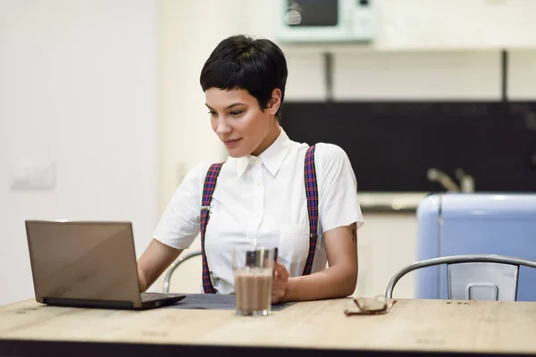 Ung kvinna med mycket kort frisyr att skriva med en bärbar dator hemma — Stockfoto