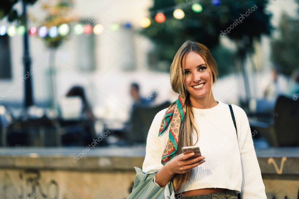 Woman with defocused urban city lights with smartphone.