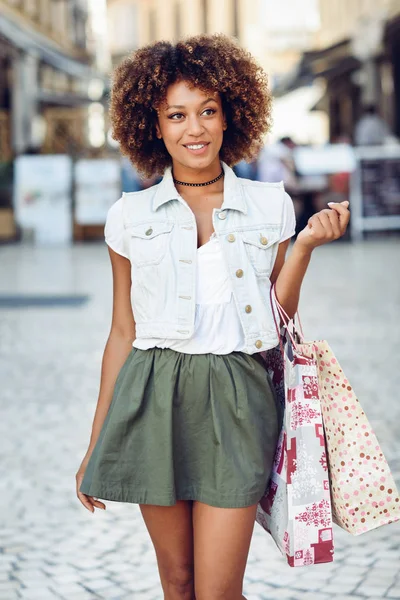 Zwarte vrouw, afro kapsel, met boodschappentassen in de straat. — Stockfoto
