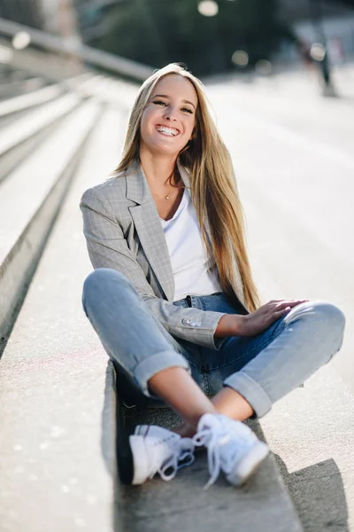 Bella giovane donna bionda sorridente sui gradini urbani . — Foto Stock