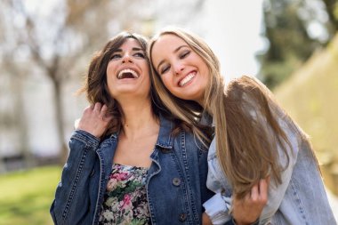 Two happy young women friends hugging in the street. clipart