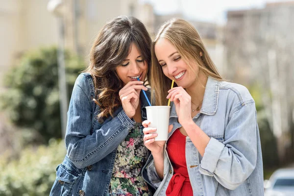 Deux jeunes femmes buvant la même boisson avec deux pailles — Photo