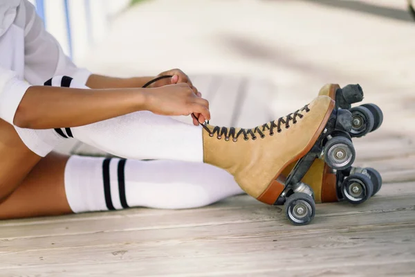 Close-up of black girl sitting on wooden floor puts on skates. — Stock Photo, Image
