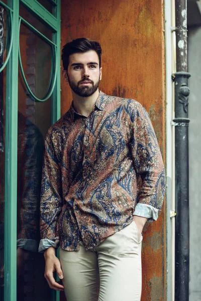 Молодой бородатый мужчина, модель моды, одет в рубашку в городской задней части — стоковое фото