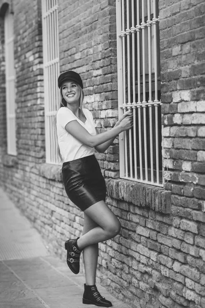 Mujer rubia joven con gorra sonriendo cerca de una pared de ladrillo . — Foto de Stock