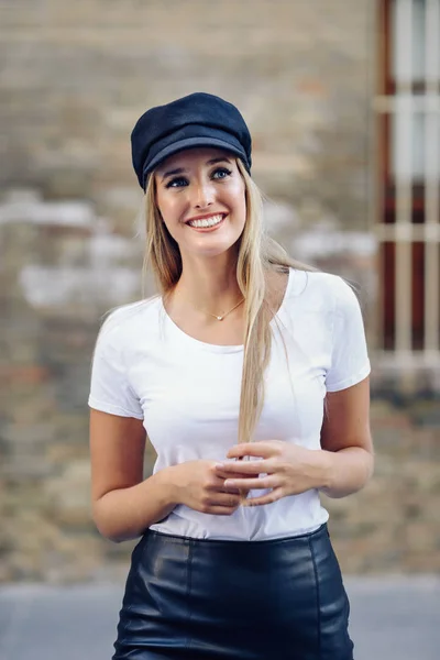 Jeune femme blonde coiffée d'un bonnet souriant près d'un mur de briques . — Photo