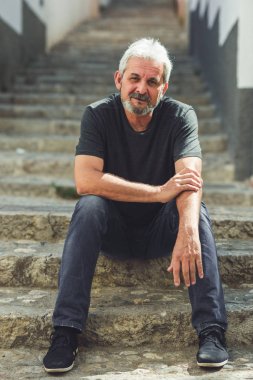 Kentsel basamaklarında oturan beyaz saçlı olgun adam