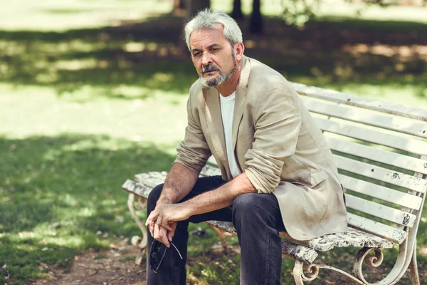 Pensive mature man sitting on bench in an urban park. — Stock Photo, Image