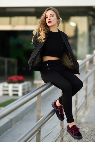 Schönes junges Mädchen in schwarzer Jacke sitzt auf der Straße. — Stockfoto