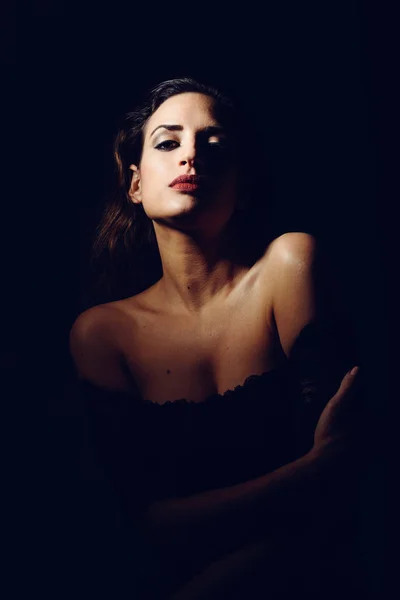 Young brunette woman in black lingerie in chiaroscuro lighting — Stock Photo, Image