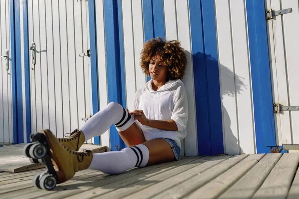 Jovem mulher negra em patins sentados perto de uma cabana de praia . — Fotografia de Stock