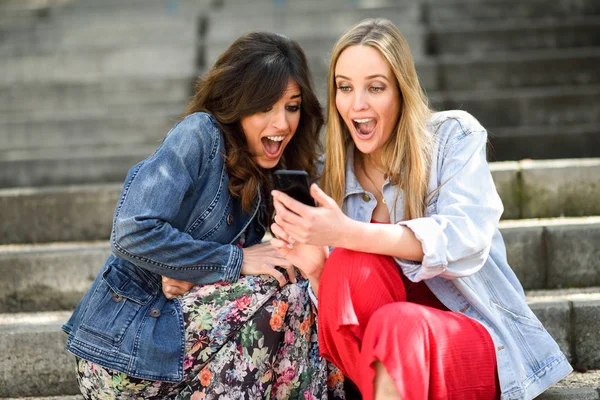 Twee jonge vrouwen op zoek naar een geweldig ding op hun slimme telefoon — Stockfoto