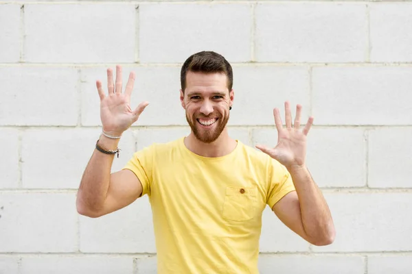 Divertente giovane uomo sul muro di mattoni con le mani aperte sorridente . — Foto Stock