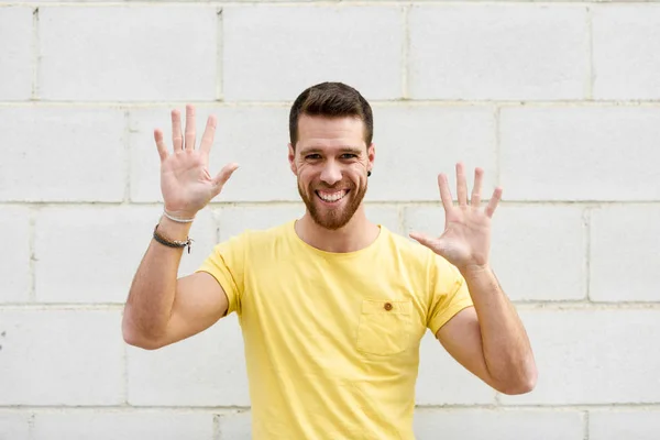 Joven gracioso en la pared de ladrillo con las manos abiertas sonriendo . — Foto de Stock