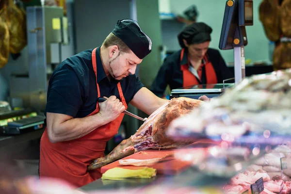 Butchers boning a ham in a modern butcher shop — ストック写真