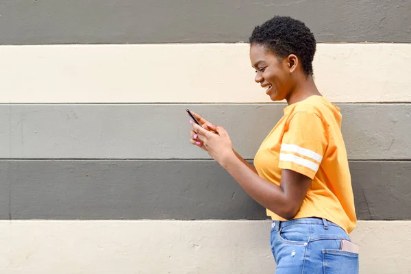 Jonge zwarte vrouw lachen met behulp van haar smartphone buiten — Stockfoto