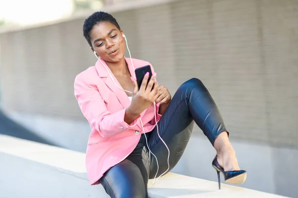 Empresaria negra sentada al aire libre hablando vía videoconferencia con su smartphone . —  Fotos de Stock